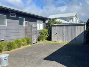 A residential property with a paved driveway, a wooden fence, and a house with a grey exterior. - Pye-a-Nui, a peaceful retreat at Whangamata beach. (Whangamatā)