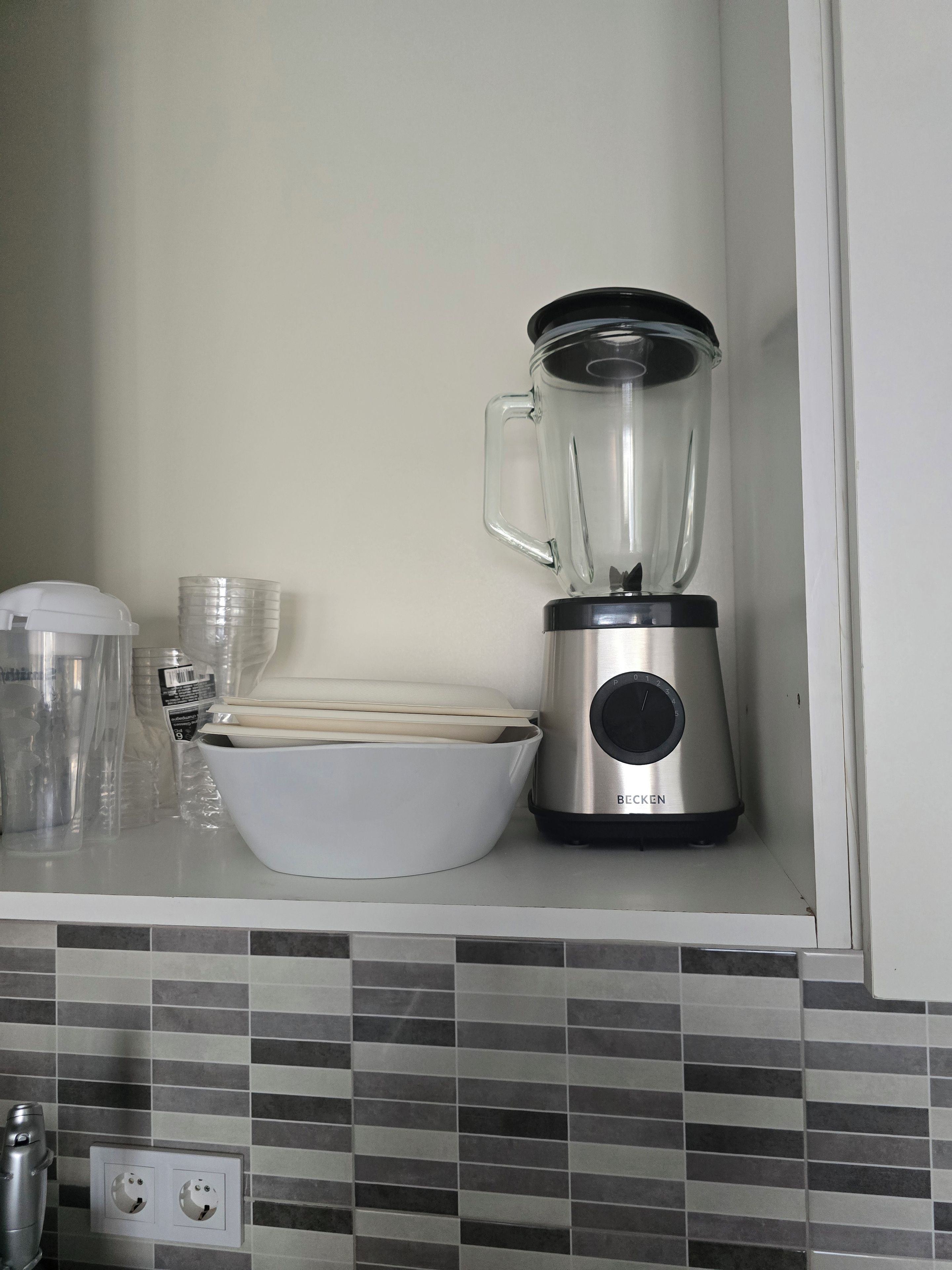 Une cuisine équipée d’un mixeur, d’un saladier blanc et de boîtes en plastique empilées sur le plan de travail.