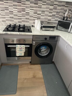 Une cuisine équipée d’une cuisinière, d’un four, d’un four à micro-ondes et d’un lave-linge à chargement frontal.