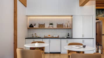 A modern kitchen with white cabinetry, a black countertop, and a wooden ceiling. There are two round tables with chairs, and a small island with a sink.