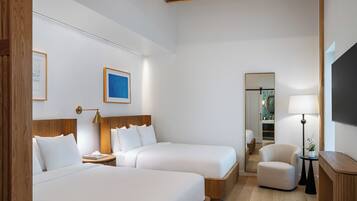 A hotel room with two beds, a sitting area, a mirror, and a TV.