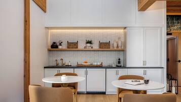 A modern kitchen with white cabinetry, a black countertop, and a wooden ceiling. There are two round tables with chairs, and a small island with a sink.