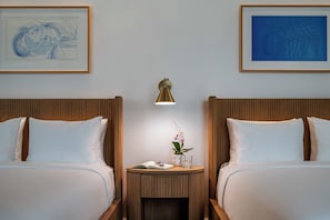 Habitación de hotel con dos camas, una mesita de noche con una lámpara, un cuadro enmarcado sobre la cama y una pequeña mesa con una planta y un vaso de agua.