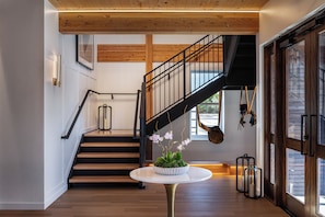 Un interior moderno con una escalera de madera, una mesa redonda con una planta en maceta y un ventanal con vistas.