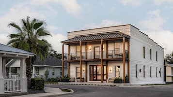 A two-story building with a balcony and a porch, featuring a brick facade and a flat roof.