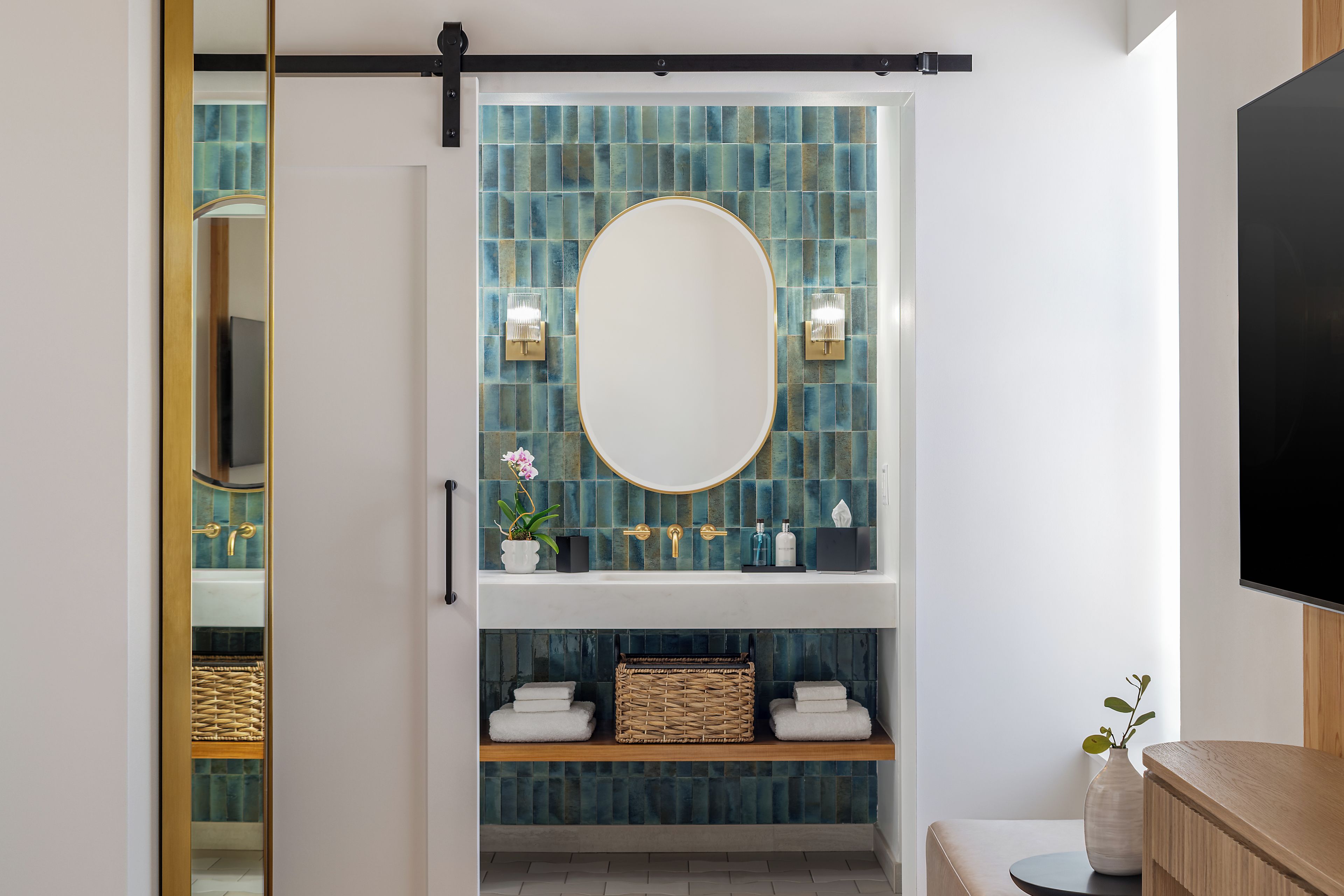 Um banheiro com um espelho grande, parede revestida de azulejos azuis e uma prateleira com toalhas e um cesto.