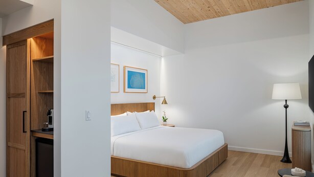 Una habitación de hotel con cama, mesita de noche, lámpara y un armario de madera.