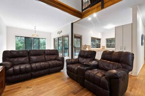 A spacious living area with a brown leather sofa, a wooden floor, and a view of a balcony. - Sandy Paws 
Toogoom 
Beachfront (Toogoom)