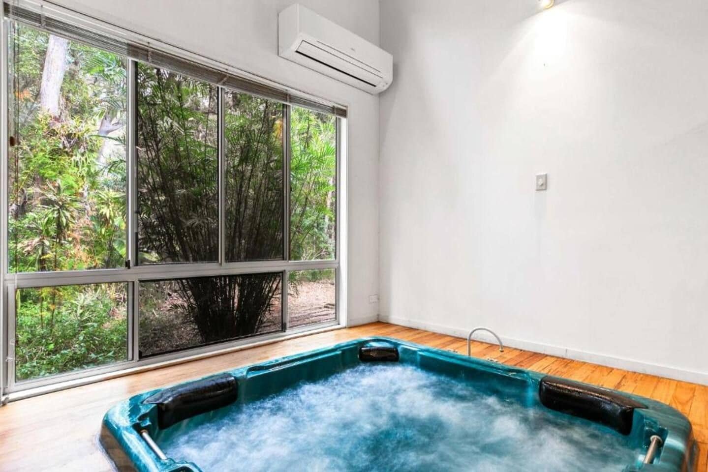 A room with a hot tub, large windows, and an air conditioning unit.