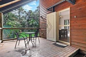 A wooden deck with a table and chairs, a sliding glass door, and a view of greenery. - Sandy Paws 
Toogoom 
Beachfront (Toogoom)