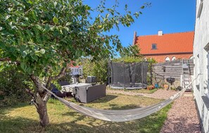 Eine Hängematte zwischen Bäumen, ein überdachter Sitzbereich und ein Gebäude mit rotem Dach im Hintergrund.