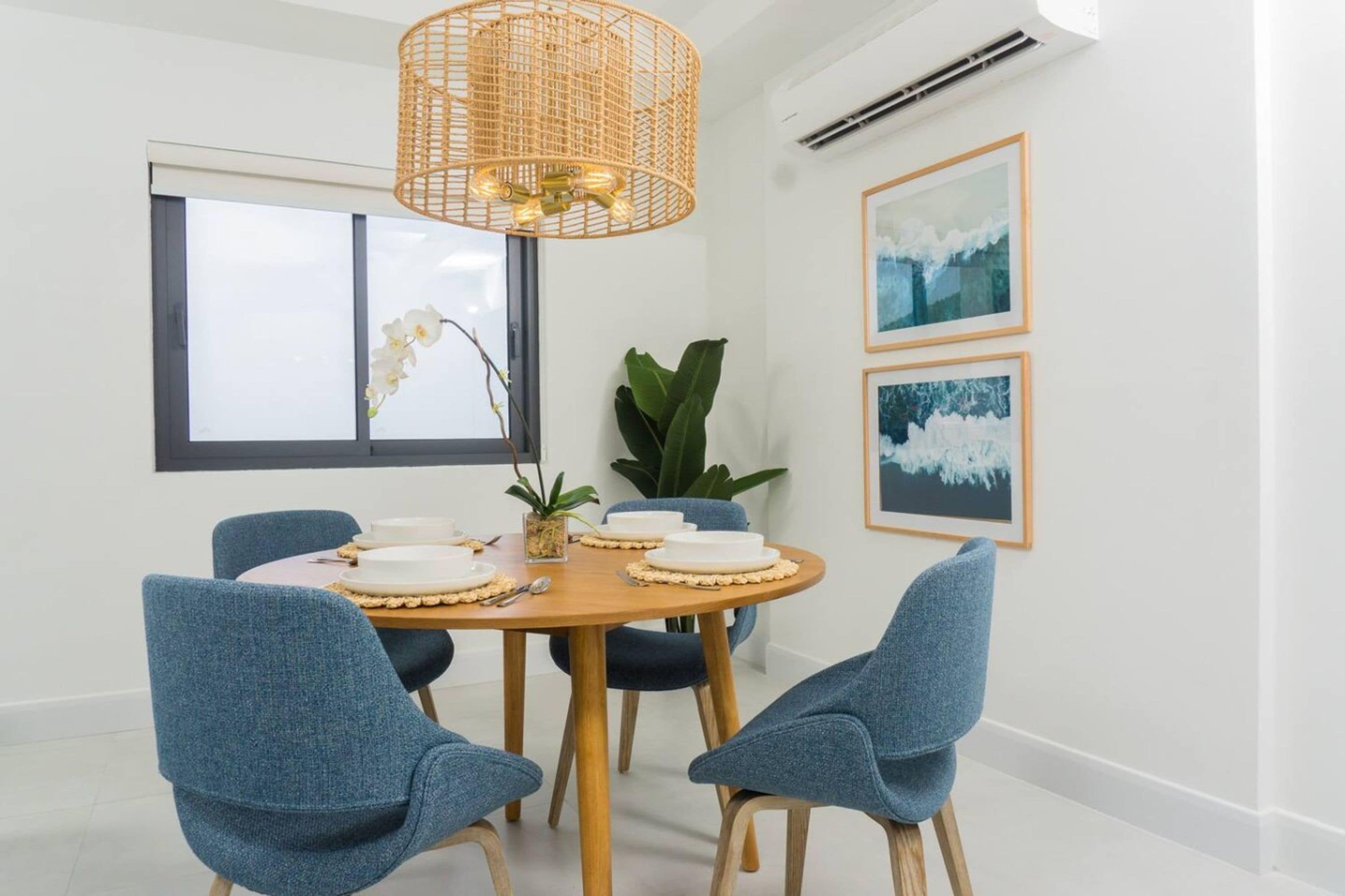 A dining area with a round table, four chairs, a hanging light fixture, and two framed pictures on the wall.