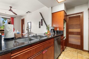 A kitchen with wooden cabinets, a stainless steel dishwasher, a granite countertop, and a ceiling fan. - 🏖️Ground-Floor Waikoloa Condo | Corner Unit + Spacious Lanai (Waikoloa)