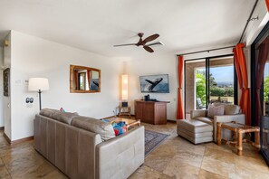 A modern living room with a sofa, a coffee table, a TV, a ceiling fan, and a view of the outdoors. - 🏖️Ground-Floor Waikoloa Condo | Corner Unit + Spacious Lanai (Waikoloa)