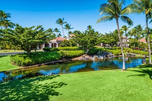 A landscaped area with a pool, palm trees, and a building with a red roof. - 🏖️Ground-Floor Waikoloa Condo | Corner Unit + Spacious Lanai (Waikoloa)