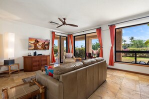 A spacious living room with a large sofa, a ceiling fan, and a television mounted on the wall. - 🏖️Ground-Floor Waikoloa Condo | Corner Unit + Spacious Lanai (Waikoloa)