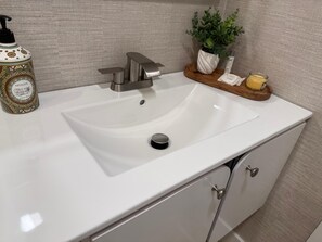 Een wastafel met een moderne kraan, een zeepdispenser en een plant in een pot op het aanrecht.
