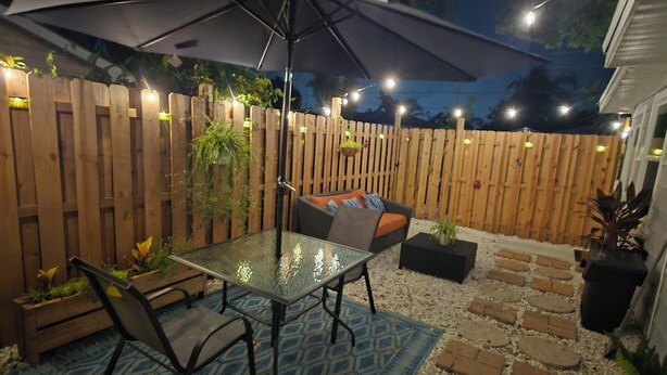 An outdoor patio area with a glass-top table, chairs, a patterned rug, and a wooden fence. - Sunrise at Sarasota (Sarasota)