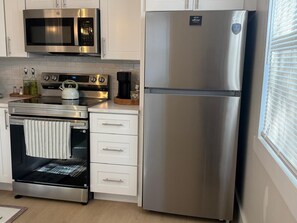 A modern kitchen with stainless steel appliances, including a microwave, oven, and refrigerator, and a window with blinds. - Sunrise at Sarasota (Sarasota)