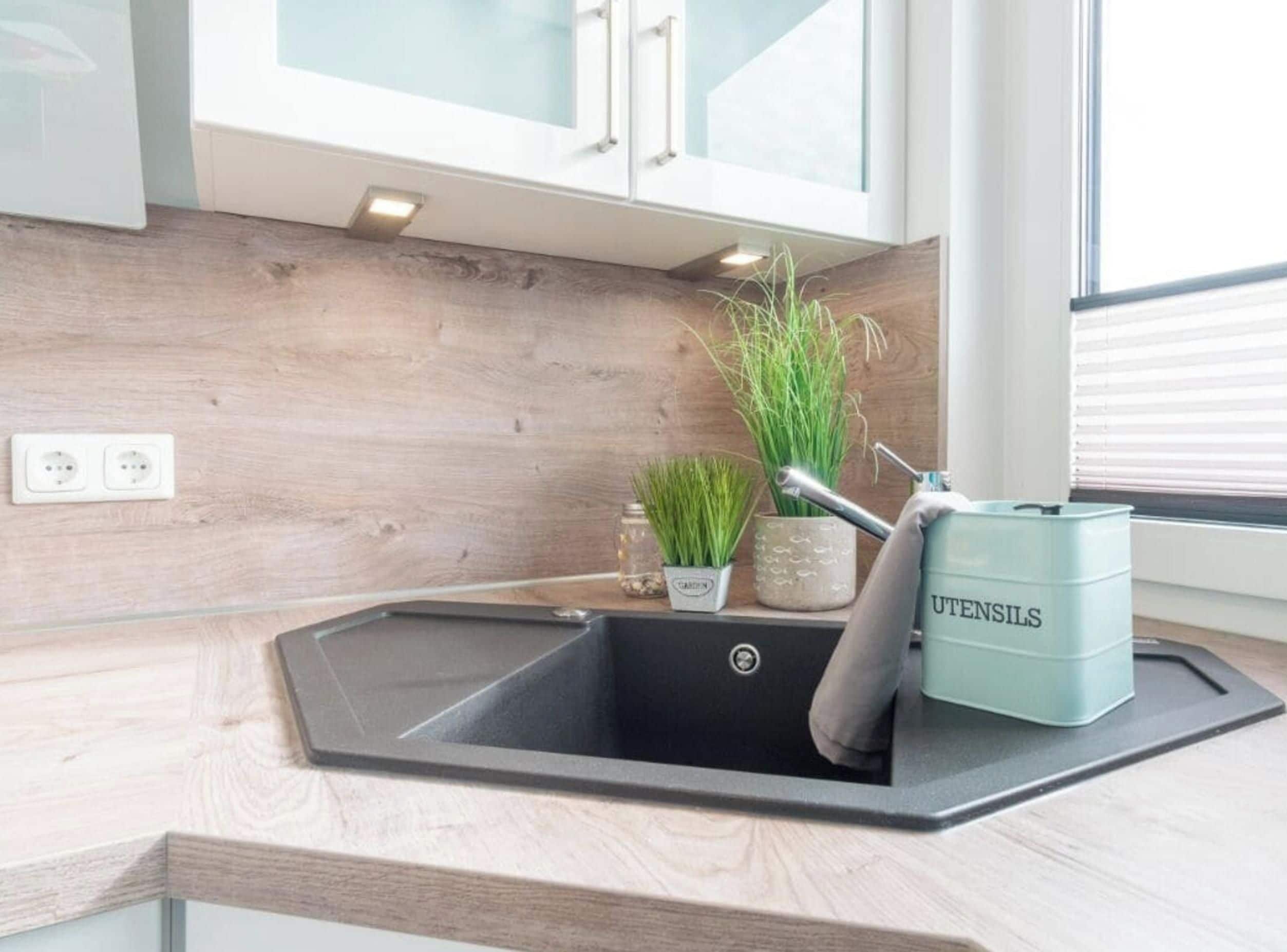 A kitchen with a black sink, wooden backsplash, and a light blue utensil container.