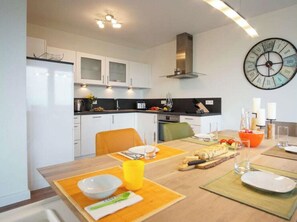 A modern kitchen with white cabinets, a black countertop, and a large wall clock. - Holiday Apartment With 2 Bedrooms (Heiligenhafen)