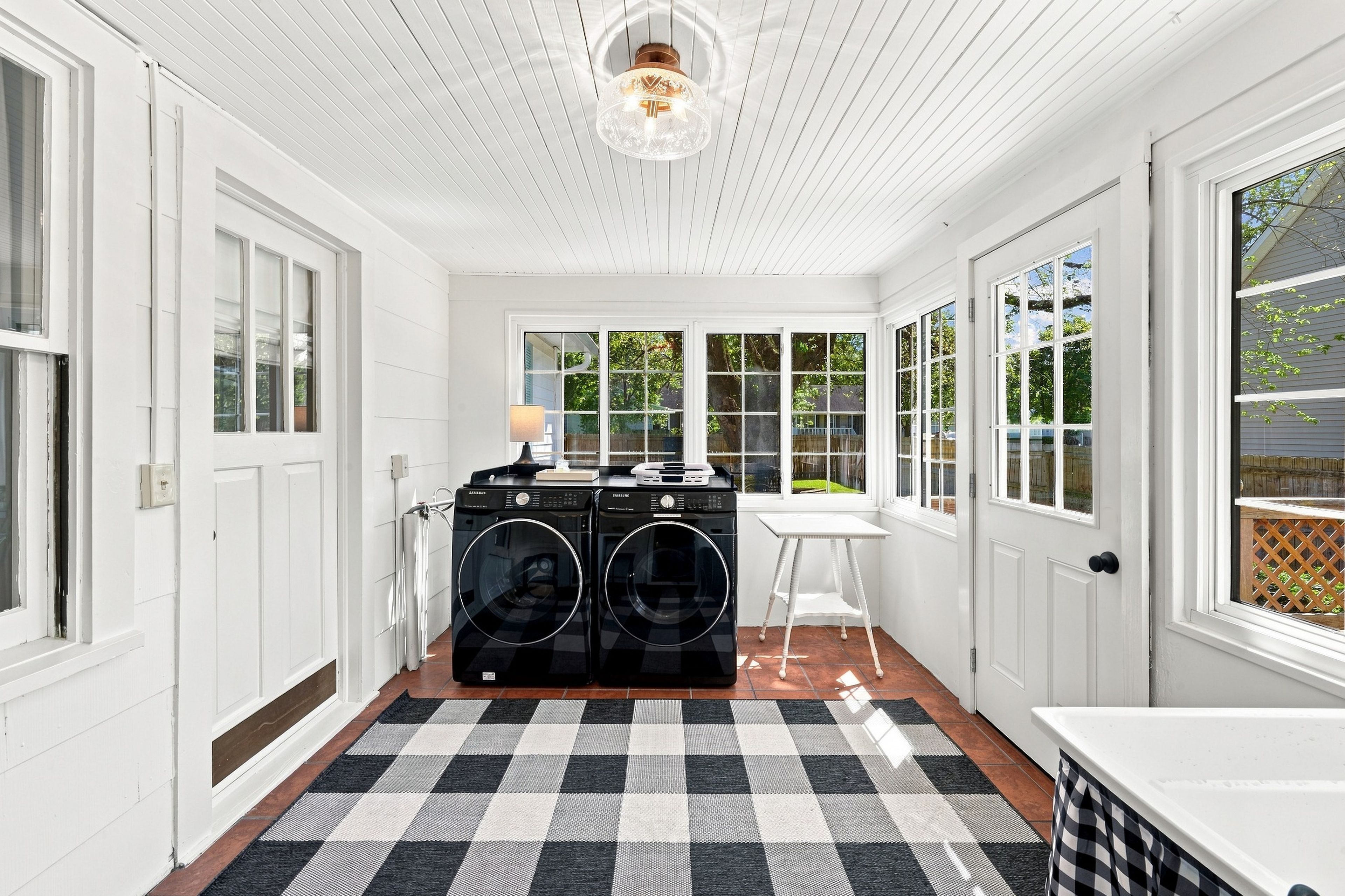 A laundry room with two black washing machines, a table, and a lamp.