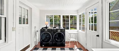 A laundry room with two black washing machines, a table, and a lamp.