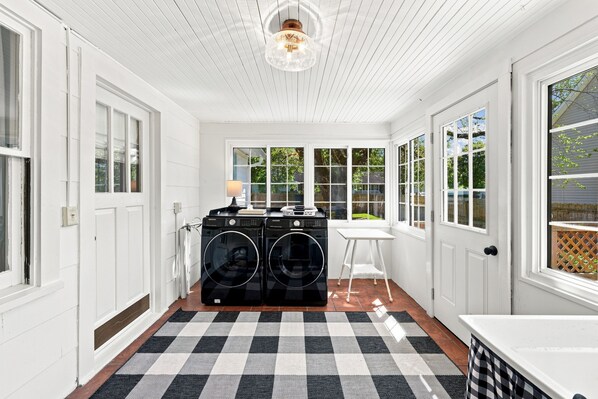 A laundry room with two black washing machines, a table, and a lamp. - Cutest 3 BR cottage in New Bern close to everything! Welcome to the New Bernian! (New Bern)