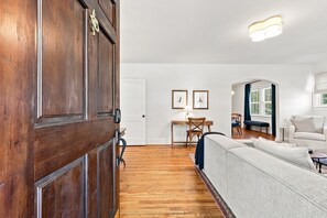 Amplia sala de estar con puerta de madera, un sofá, una mesa de comedor con sillas y vistas al exterior a través de una ventana.