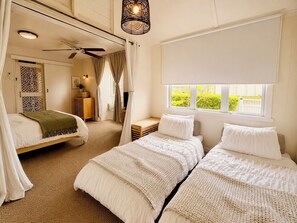 Ein Schlafzimmer mit zwei Betten, einem Deckenventilator, einem Fenster mit Blick und einer dekorativen Leuchte.