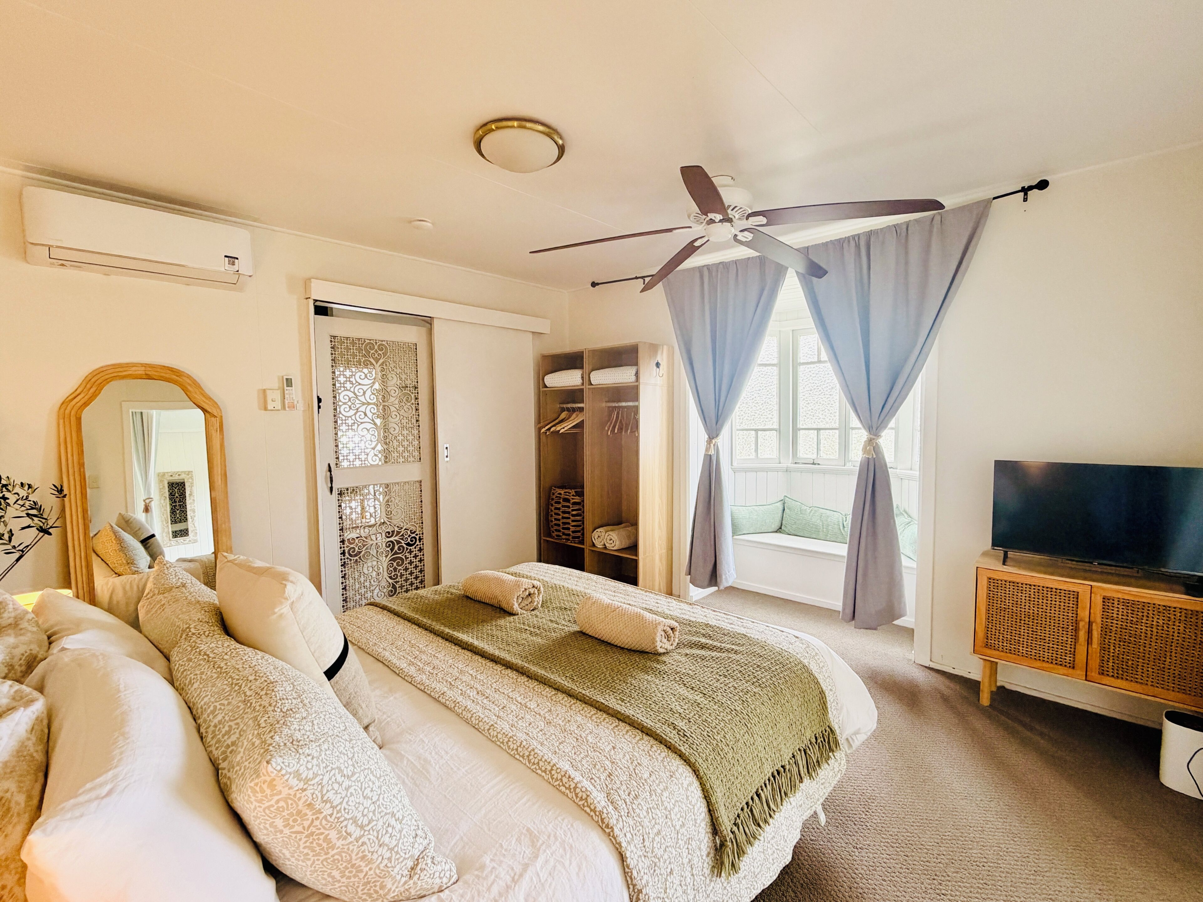 Une chambre à coucher avec un lit, une télévision, une armoire et une fenêtre avec des rideaux.