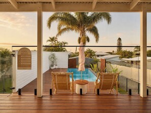 Ein Poolbereich mit Holzterrasse, zwei Korbstühlen, einem kleinen runden Tisch und einer Palme.