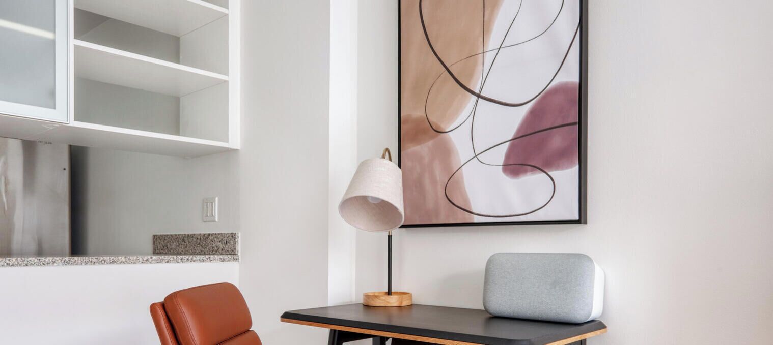 Una habitación moderna con diseño minimalista, que incluye un estante blanco, una mesa con lámpara y un sofá gris.