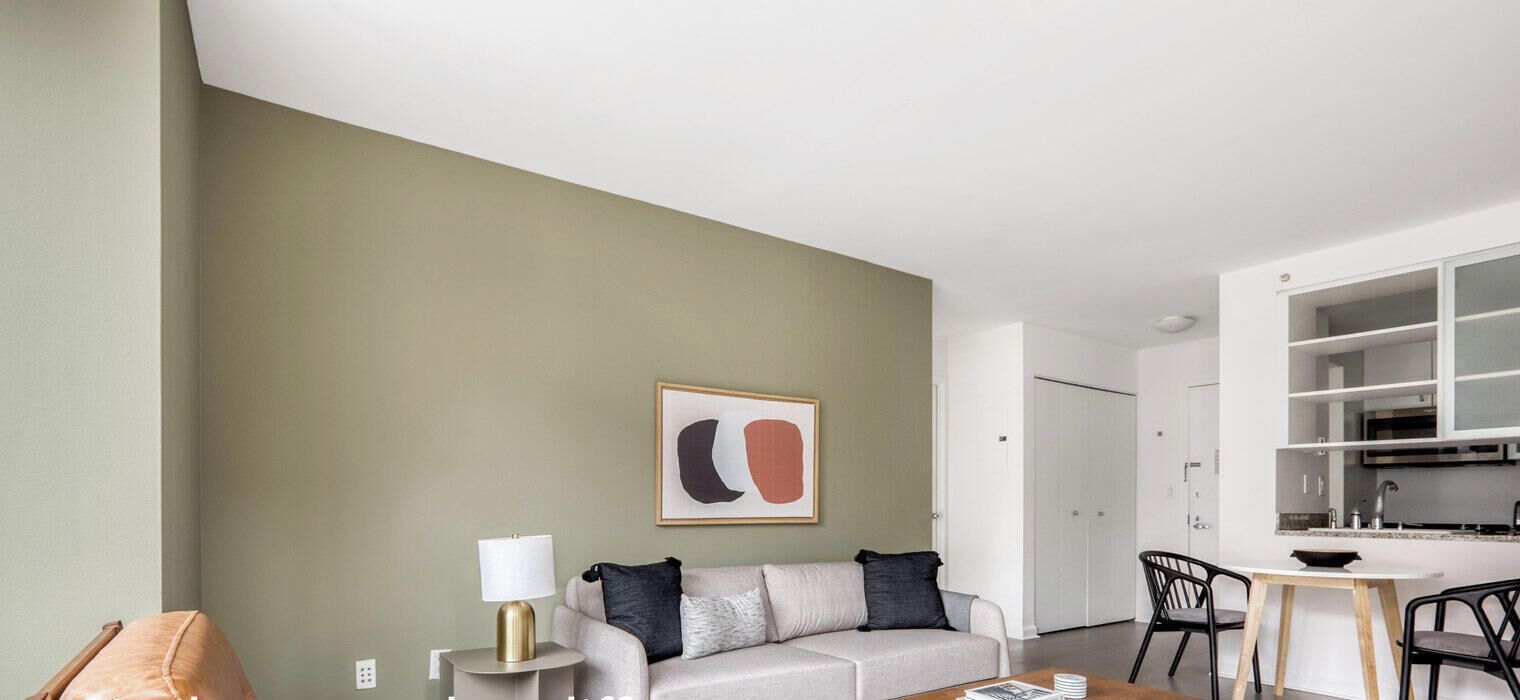 A modern living room with a sofa, a side table, a lamp, and a framed abstract artwork on the wall.