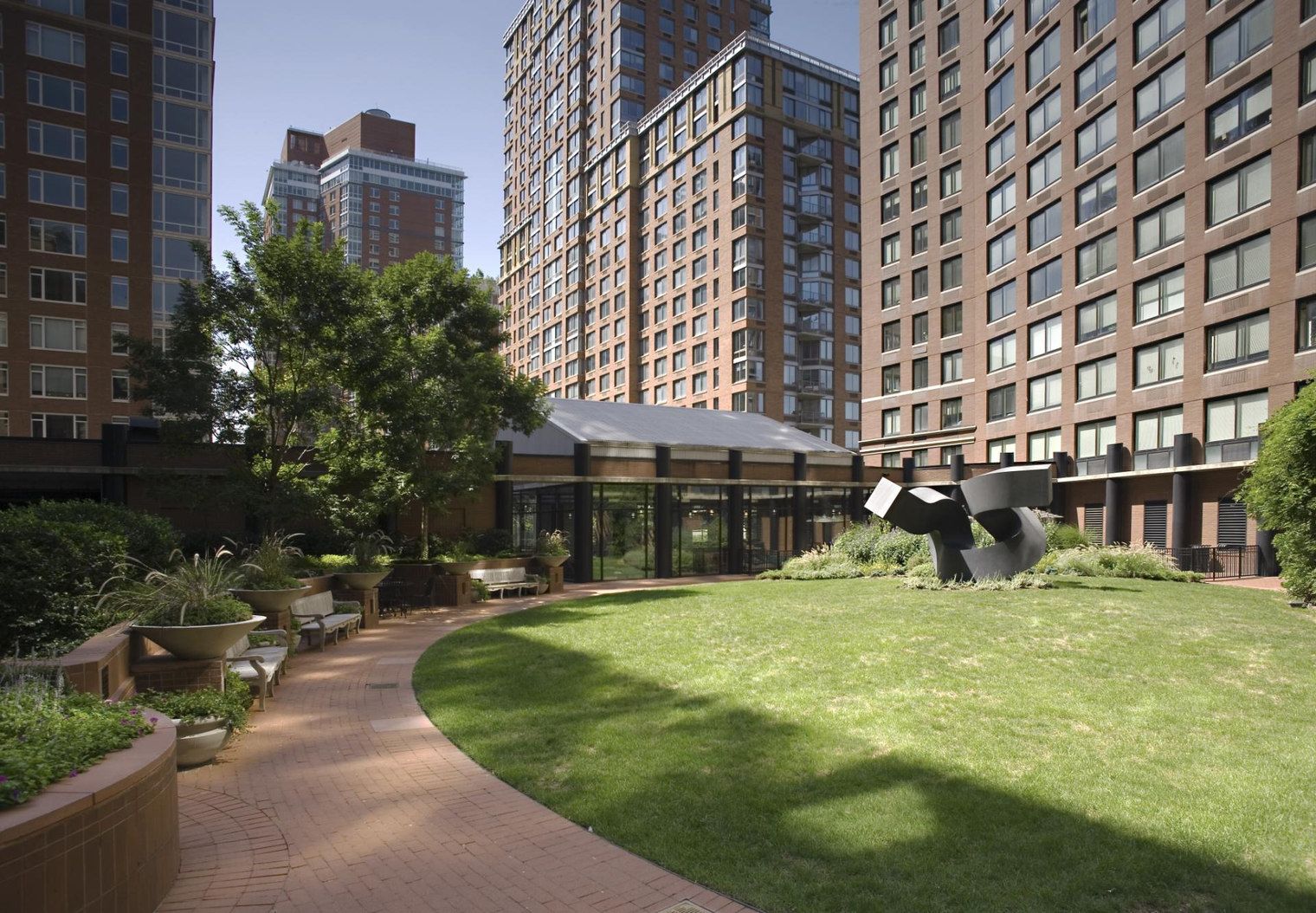A courtyard with a pathway, seating areas, and a modern sculpture.