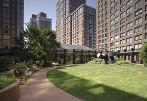 Un patio con un sendero, zonas de estar y una escultura moderna.