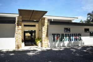 A building with a stone facade, a covered entrance, and a sign that reads "TRAINING". - Oasis Apartment in the City at the Avalon Country Club Condominium in Costa Rica (Río Oro)