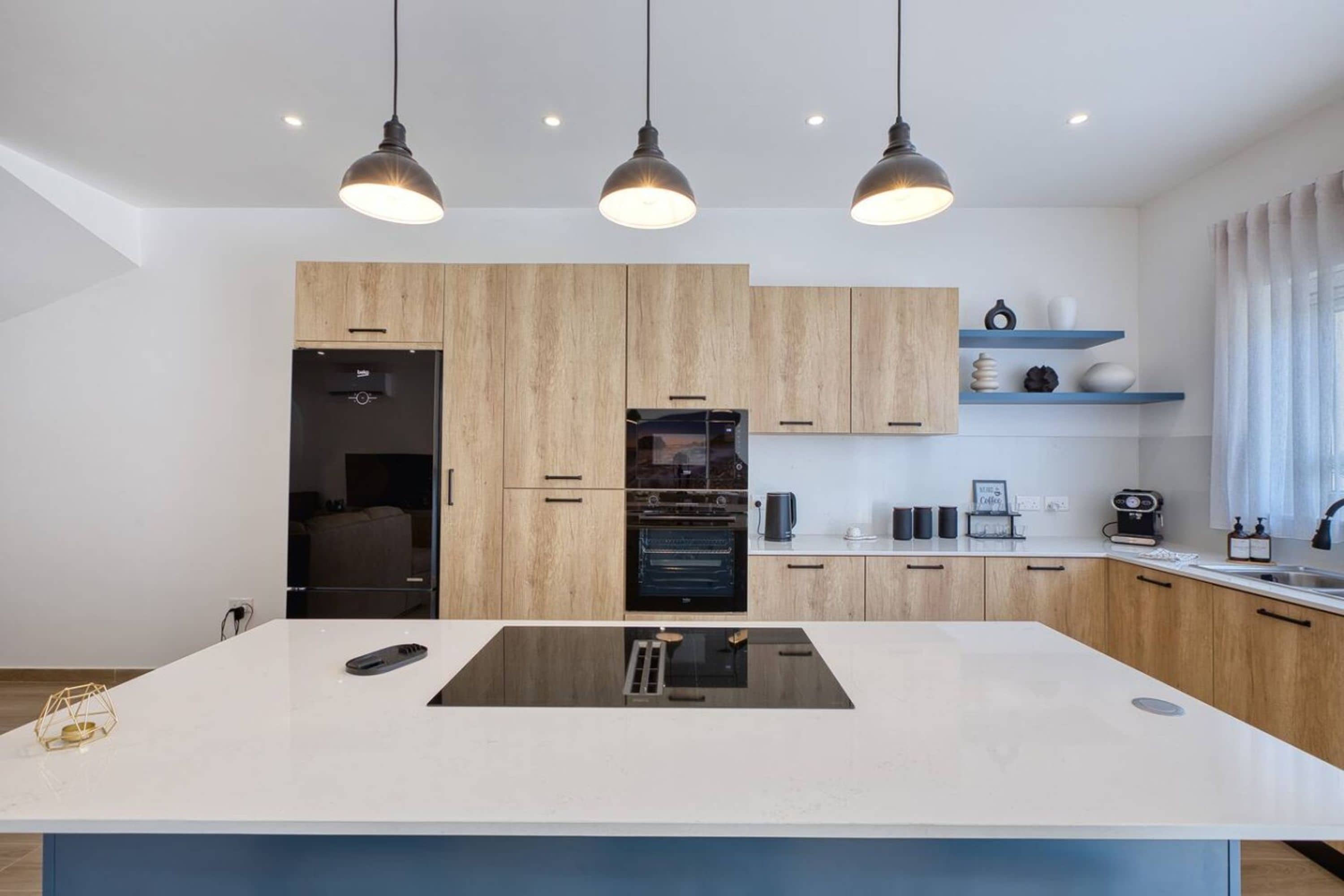 A modern kitchen with a central island, wooden cabinets, and pendant lighting.