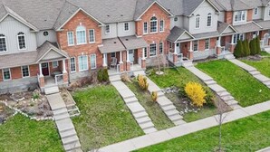 A row of two-story houses with a front yard, a driveway, and a parked car. - Billabong home (Guelph)