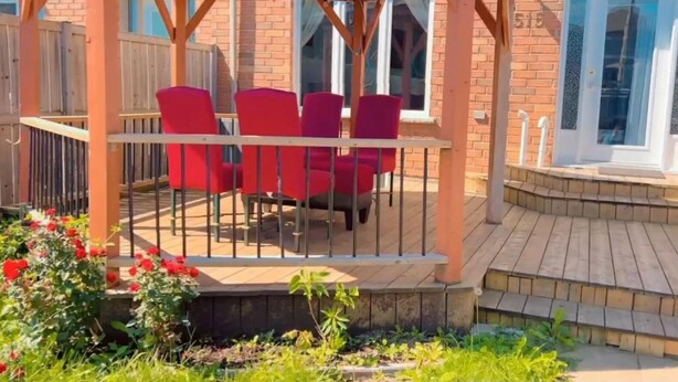A covered outdoor seating area with a wooden pergola, red chairs, and a brick building in the background. - Billabong home (Guelph)