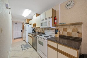 A kitchen with white appliances, a microwave, stove, and a clock on the wall. - San-A-Bel Oceanfront Getaway | 2BR (North Myrtle Beach)