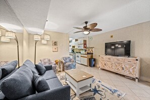A living room with a sofa, a coffee table, a television, and a ceiling fan. - San-A-Bel Oceanfront Getaway | 2BR (North Myrtle Beach)