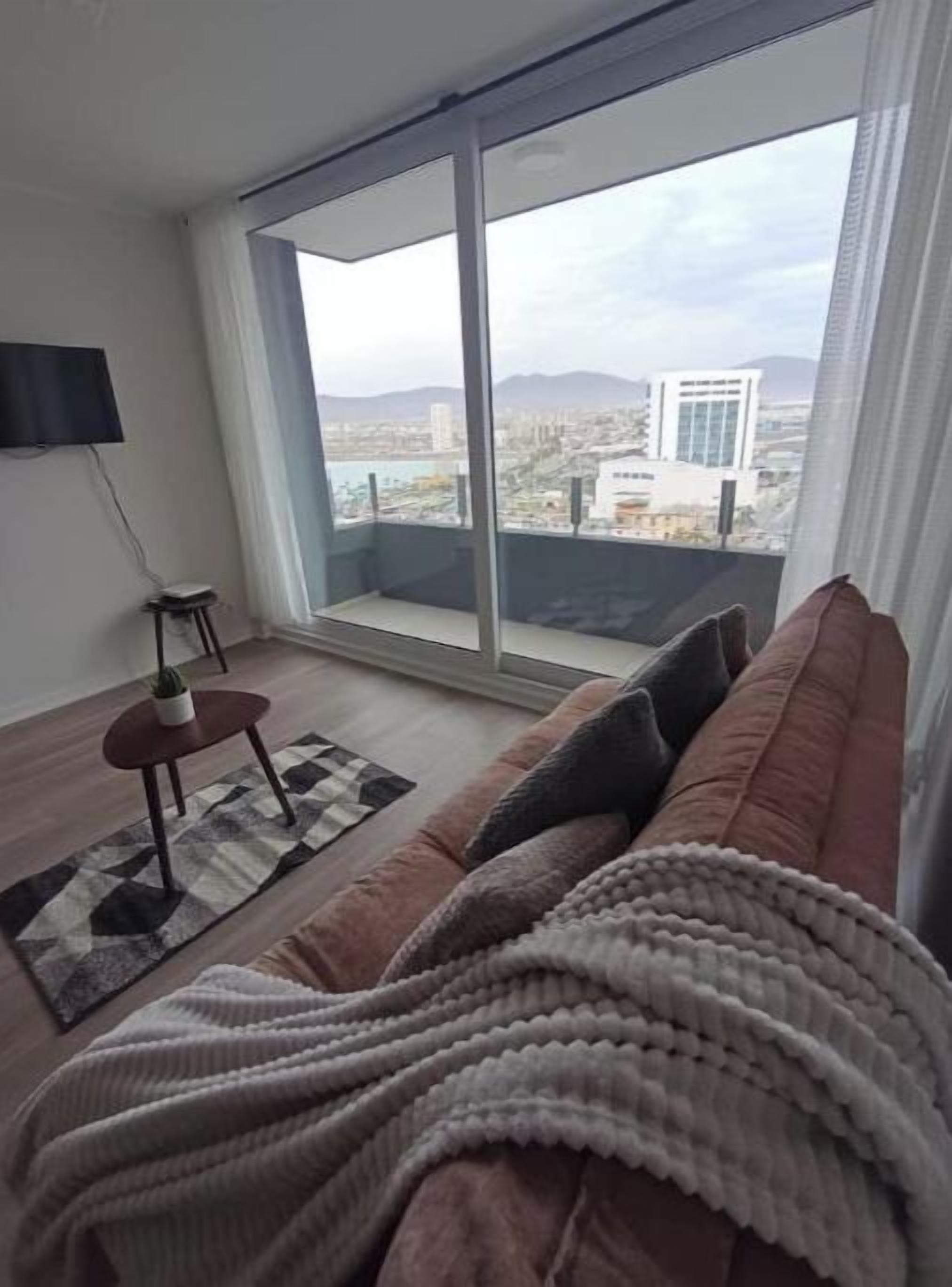 Una sala de estar moderna con un ventanal grande, un sofá, una mesita y un televisor.