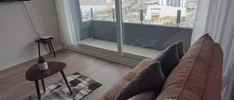 Una sala de estar moderna con un ventanal grande, un sofá, una mesita y un televisor.