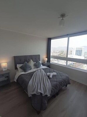 A bedroom with a large window, a bed with a grey quilt, and a city view. - Apartment with an ocean view across from the harbor/downtown (Coquimbo)