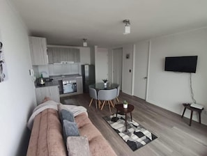 A modern living room with a sofa, a dining table with chairs, a kitchen area, and a flat-screen TV mounted on the wall. - Apartment with an ocean view across from the harbor/downtown (Coquimbo)