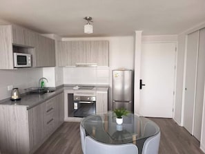 A modern kitchen with grey cabinets, a stainless steel refrigerator, a microwave, and a glass-top table with a potted plant. - Apartment with an ocean view across from the harbor/downtown (Coquimbo)