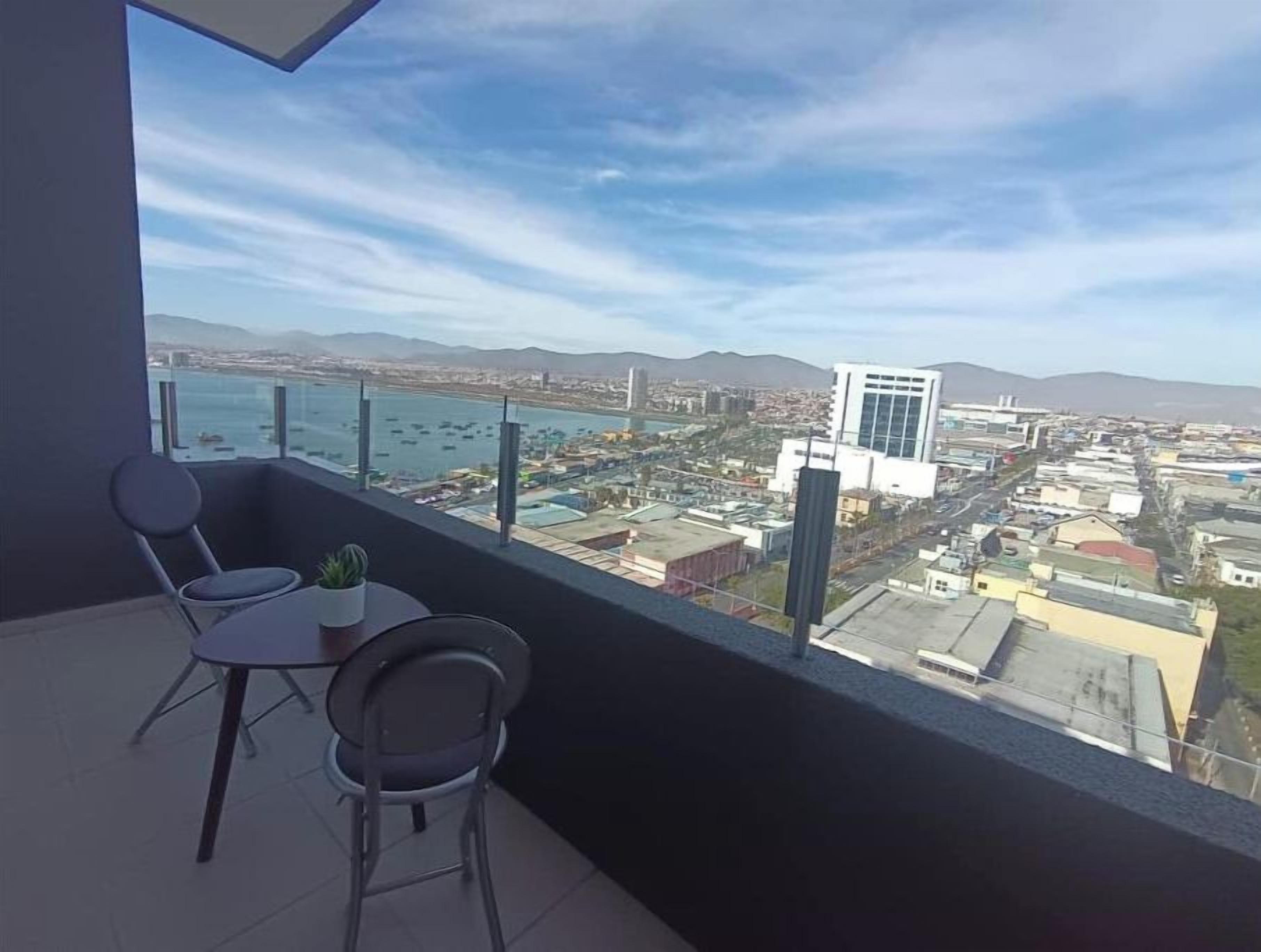A balcony with a view of a cityscape, including a body of water and mountains in the distance.