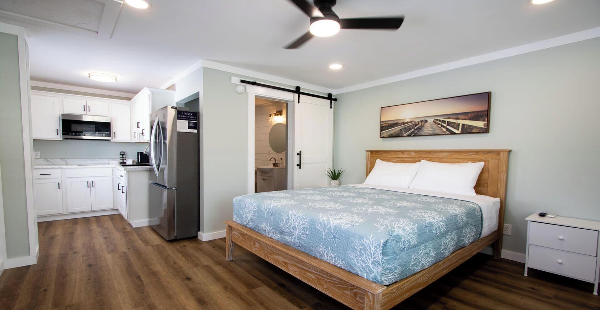 A bedroom with a bed, a ceiling fan, and a painting on the wall.