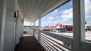 A covered porch with a view of a waterfront and a red building with signage. - ⚓ Brand New Downtown Retreat: The Lofts at Big Rock Landin (Morehead City)